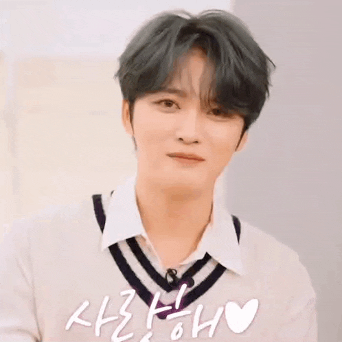 a man making a heart shape with his hands in front of a sign that says ' 사랑해 '