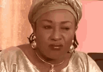 a woman wearing a turban and a necklace is making a funny face while sitting on a couch .