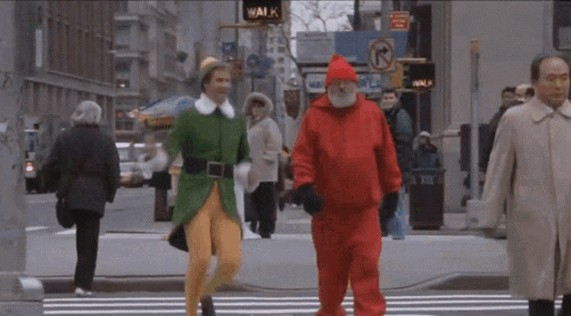 a man dressed as an elf and a man dressed as santa walk down a city street
