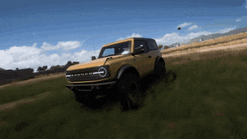 a yellow ford bronco is driving down a grassy hill