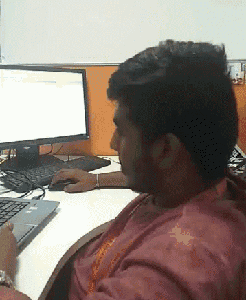 a man in a red shirt is sitting at a desk in front of a dell computer monitor