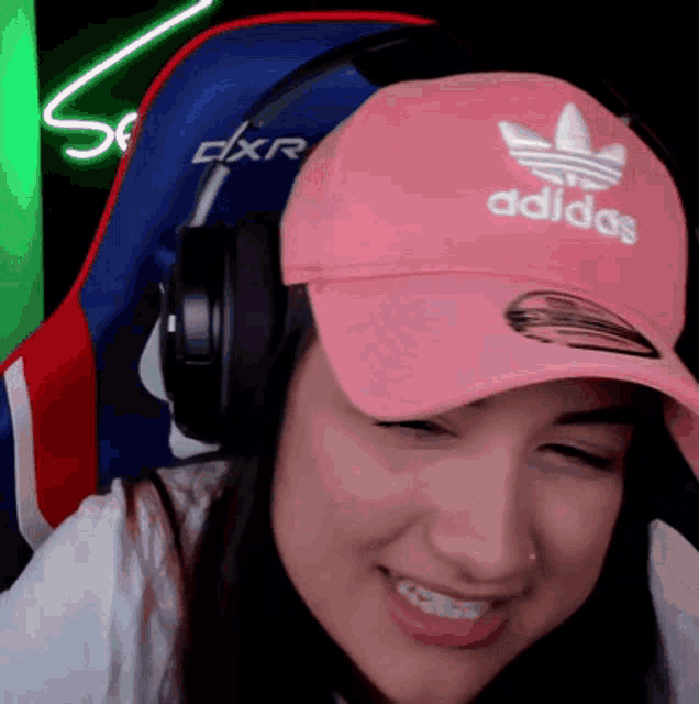a woman wearing a pink adidas hat and headphones smiles