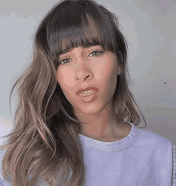 a woman with long hair and bangs is wearing a purple t-shirt