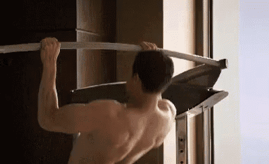 a shirtless man is doing a pull up on a bar in a room .