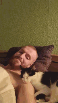 a man laying in bed with a cat on his shoulder