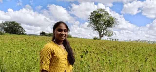a young woman in a yellow shirt is standing in a field of tall grass .