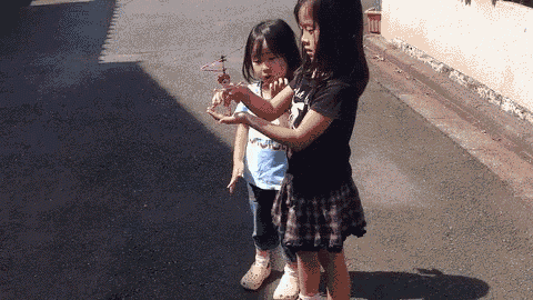 two little girls playing with a toy helicopter on a street