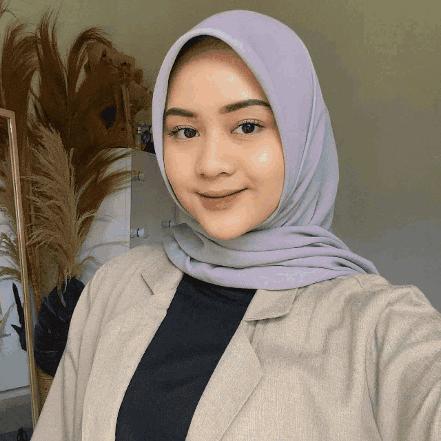 a woman wearing a purple hijab and a blazer takes a selfie