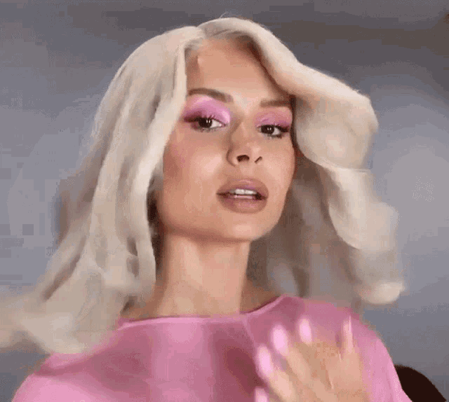 a woman with blonde hair and pink eye shadow is wearing a pink top