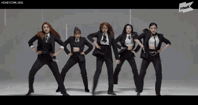 a group of women in tuxedos are dancing in front of a sign that says the k