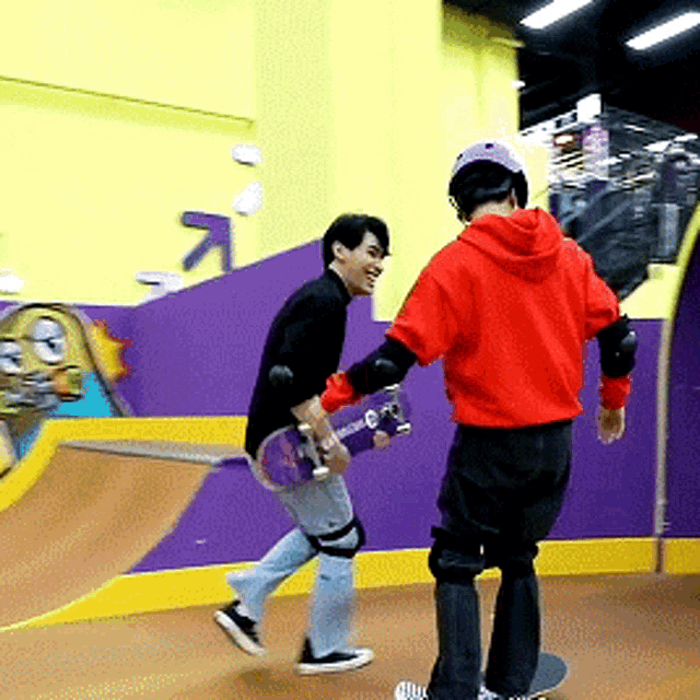 a man in a red hoodie is holding a skateboard while another man looks on