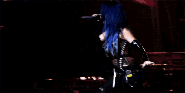a woman with blue hair singing into a microphone on stage