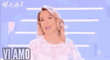 a woman in a white dress is standing in front of a blue background and says `` vi amo follemente '' .