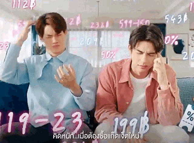 two men are sitting next to each other on a couch with numbers on the wall in the background .