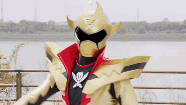 a gold and black superhero with a skull and crossbones on his chest is standing in front of a body of water