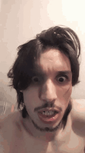 a shirtless man with long hair and a beard making a funny face