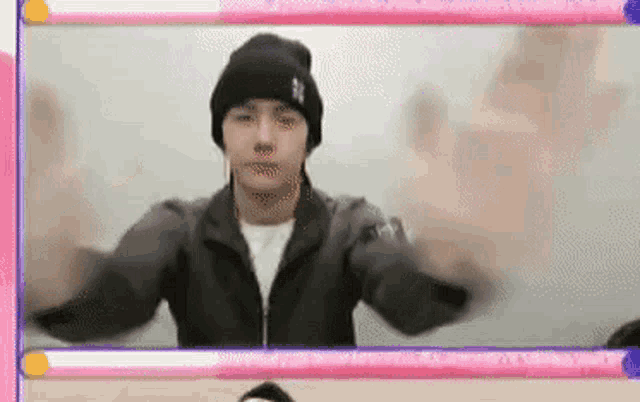 a man wearing a black beanie and a black jacket is standing in front of a mirror with his arms outstretched .