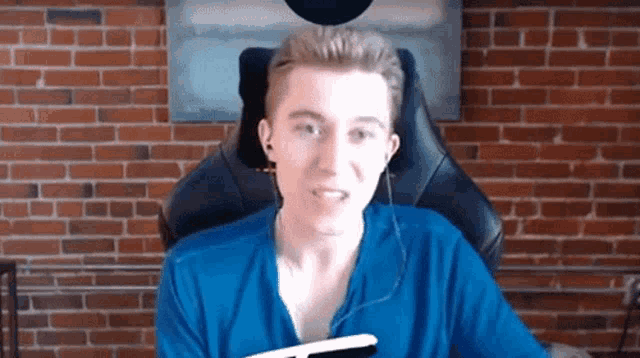 a young man in a blue shirt is sitting in a chair