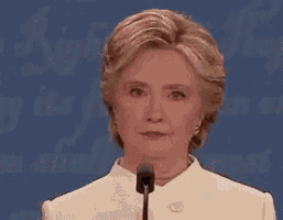 hillary clinton is speaking into a microphone in front of a blue background .