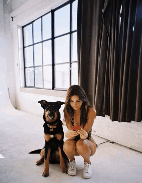 a woman kneeling next to a dog looking at her cell phone