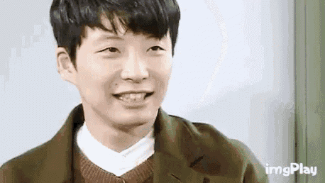 a close up of a young man wearing a green jacket and a brown sweater smiling .