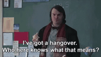 a man is standing in front of a chalkboard eating a sandwich and talking about a hangover