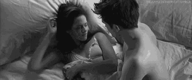 a black and white photo of a man and a woman laying in bed .