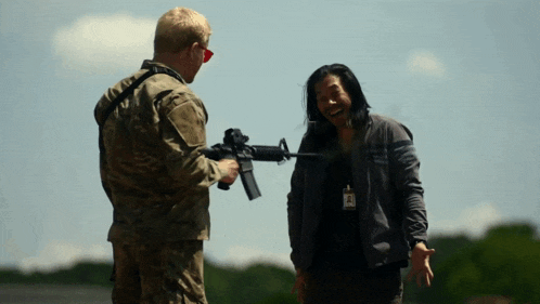 a man in a military uniform is holding a gun and talking to another man
