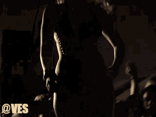 a woman in a bikini stands in a dark room with the words @ves written on the bottom