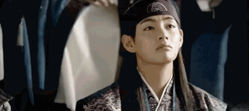 a young man in a traditional korean dress and headband is standing in a room .