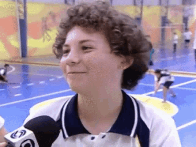 a girl with curly hair is smiling in front of a microphone that says g on it