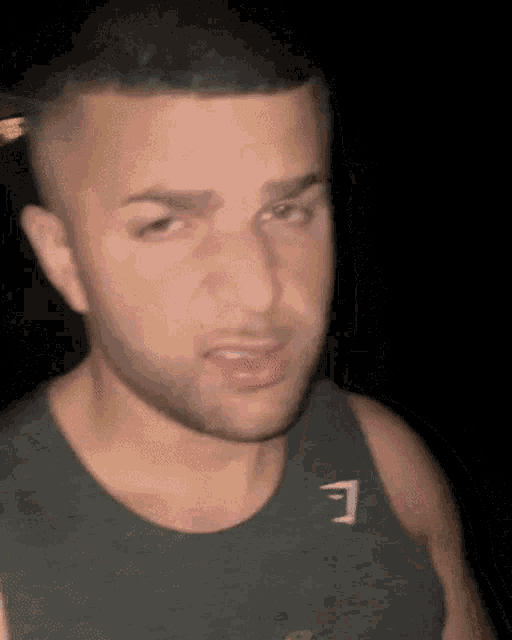 a man with a beard is wearing a tank top with the letter e on it .