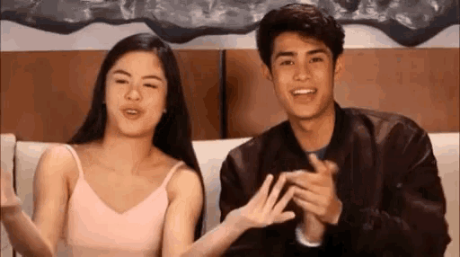 a man and a woman are sitting on a couch and clapping their hands .