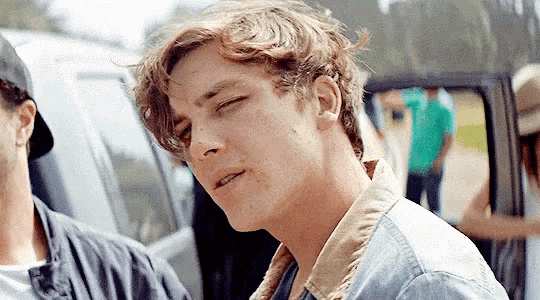 a close up of a young man 's face with his eyes closed standing next to a car .