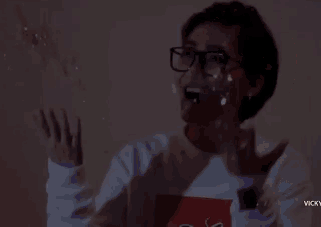 a woman wearing glasses is standing in front of a wall with confetti falling on her head .