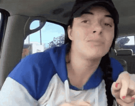 a woman wearing a hat and a blue and white shirt is sitting in the back seat of a car .