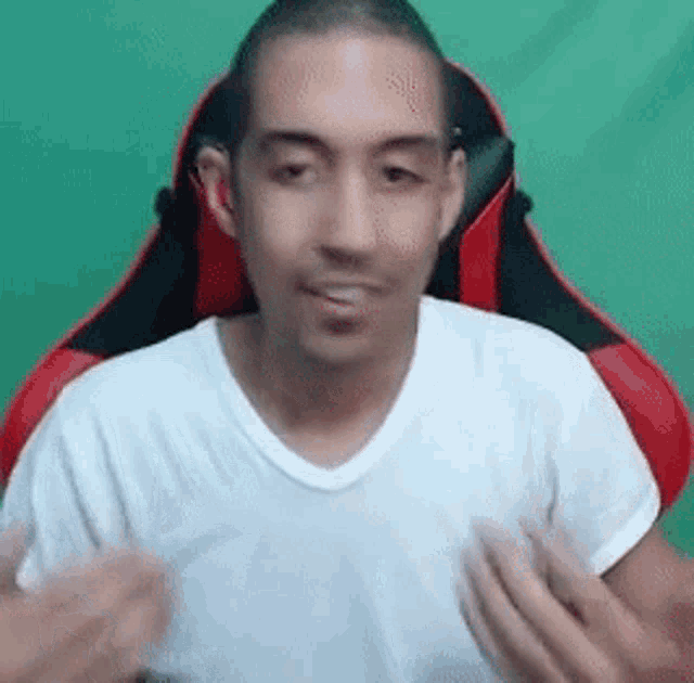 a man in a white t-shirt is sitting in a red and black gaming chair .