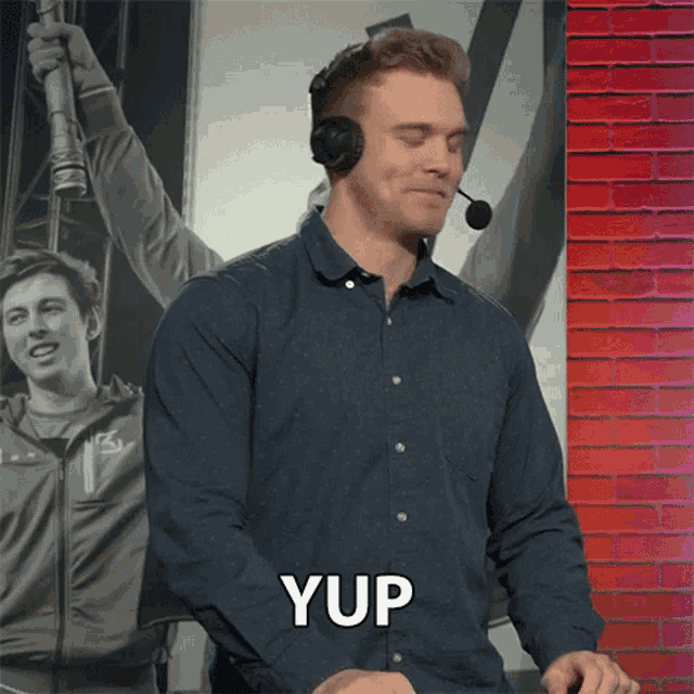 a man wearing a headset says yup in front of a red brick wall