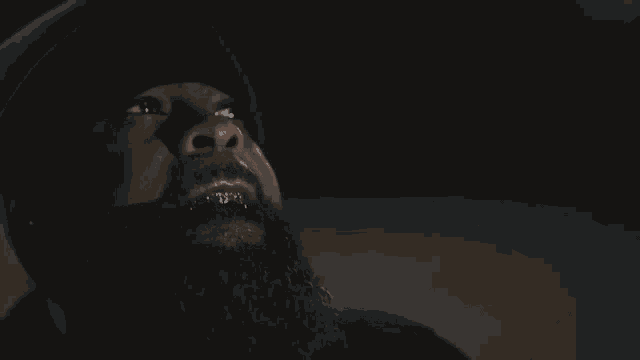 a man with a beard and gold teeth looks up at something