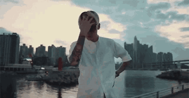 a man with tattoos on his arm is standing in front of a body of water .
