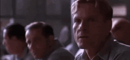 a man is sitting in a room with other men and looking at something .