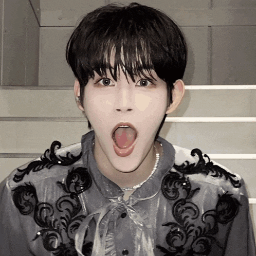 a young man with his tongue hanging out is wearing a gray shirt with black embroidery