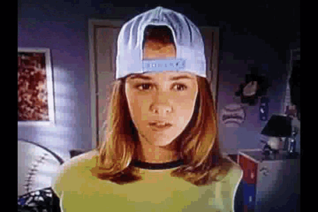 a girl wearing a baseball cap and a yellow shirt is standing in a room .