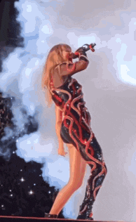 a woman in a red and black outfit is singing into a microphone on stage .