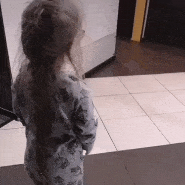 a little girl wearing a sweater with cats on it is standing on a tiled floor