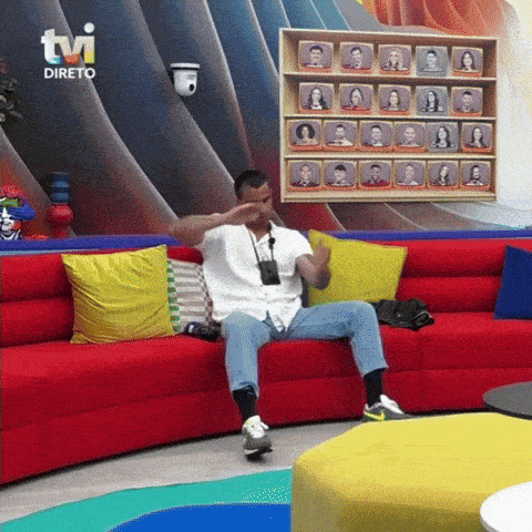 a man sits on a red couch in front of a wall that says " tvi direto "