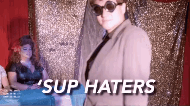 a woman wearing sunglasses and a suit says ' sup haters ' in a photo booth