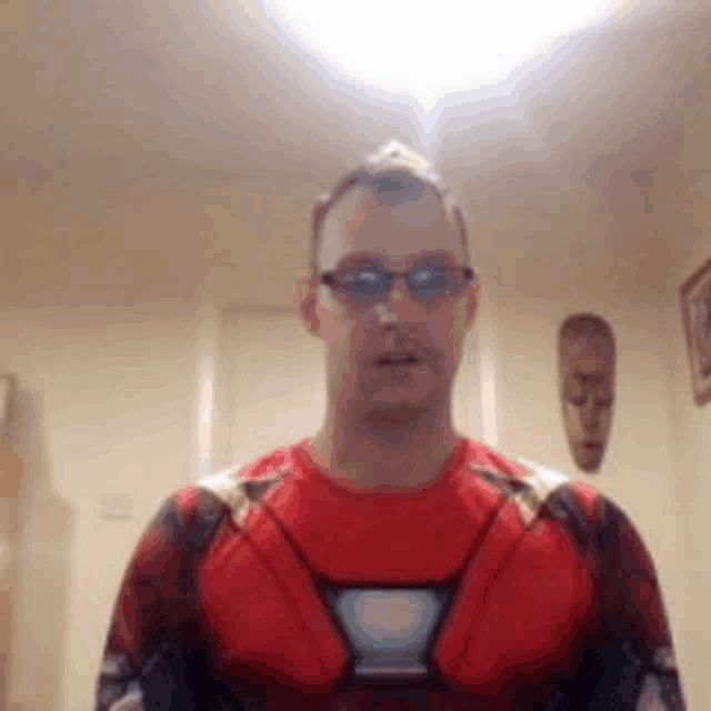 a man in a superhero costume is wearing sunglasses and standing in a room .