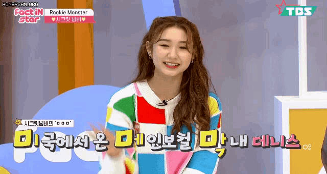 a girl is wearing a colorful sweater and smiling while talking on a television show .