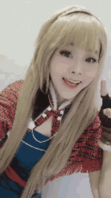 a woman with long blonde hair is wearing a plaid shirt and gloves and taking a selfie .